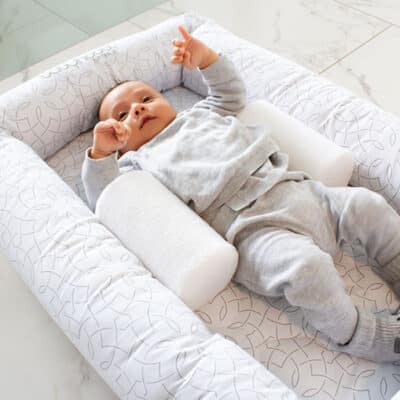 baby lying in cosy crib in mosaic print with a sleep positioner