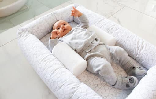 baby lying in cosy crib in mosaic print with a sleep positioner