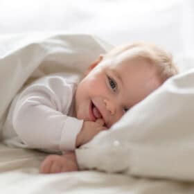 baby lying on bed smiling with thumb in its mouth