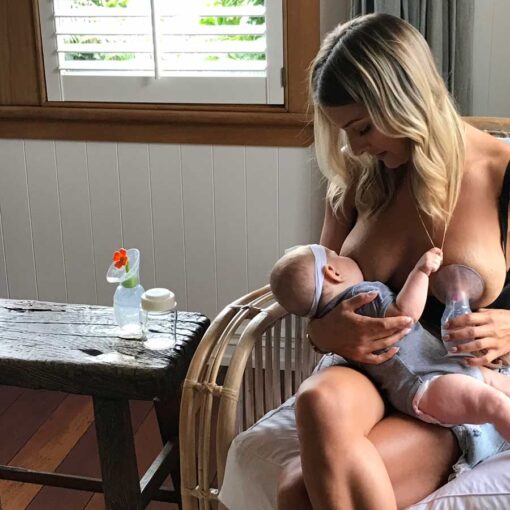 mum using haakaa silicone breast pump while breastfeeding baby