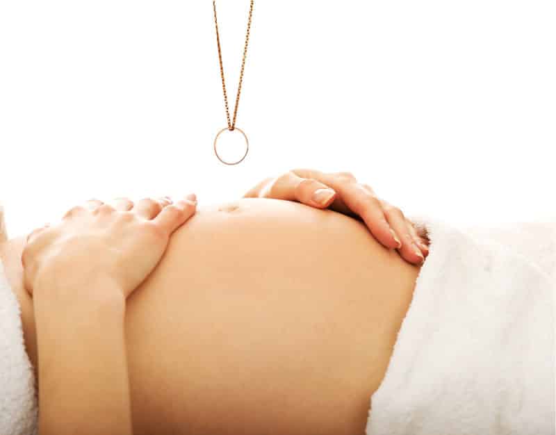 the ring test gender predictor shown by a pregnant belly with ring on necklace over the belly
